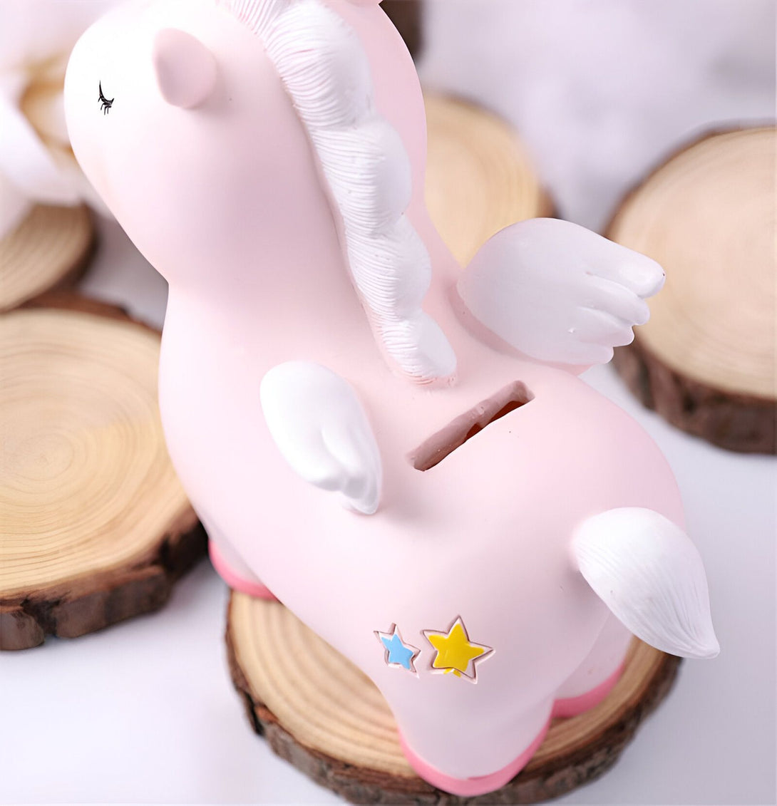 Une tirelire en forme de licorne rose avec des ailes blanches et une crinière blanche. La licorne est debout sur une bûche de bois.