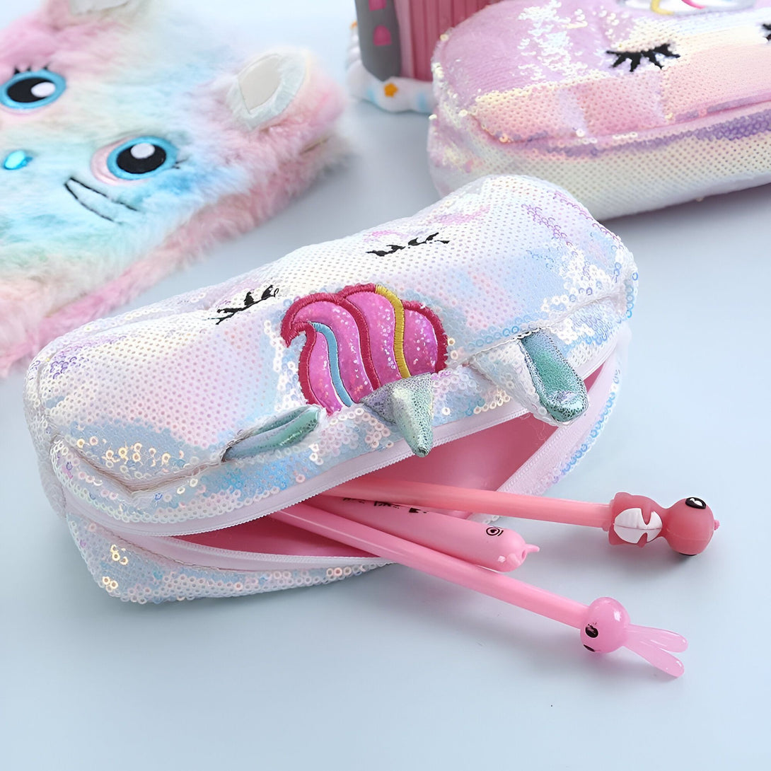 Une trousse à crayons en forme de licorne blanche et rose avec des paillettes et une fermeture éclair. Il y a des stylos et des crayons à l'intérieur de la trousse.