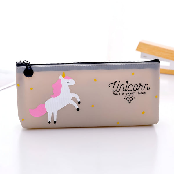 Une trousse transparente avec une licorne blanche et rose. Il y a des étoiles jaunes sur le devant de la trousse et le texte "Unicorn have a sweet dream" est écrit en lettres noires.