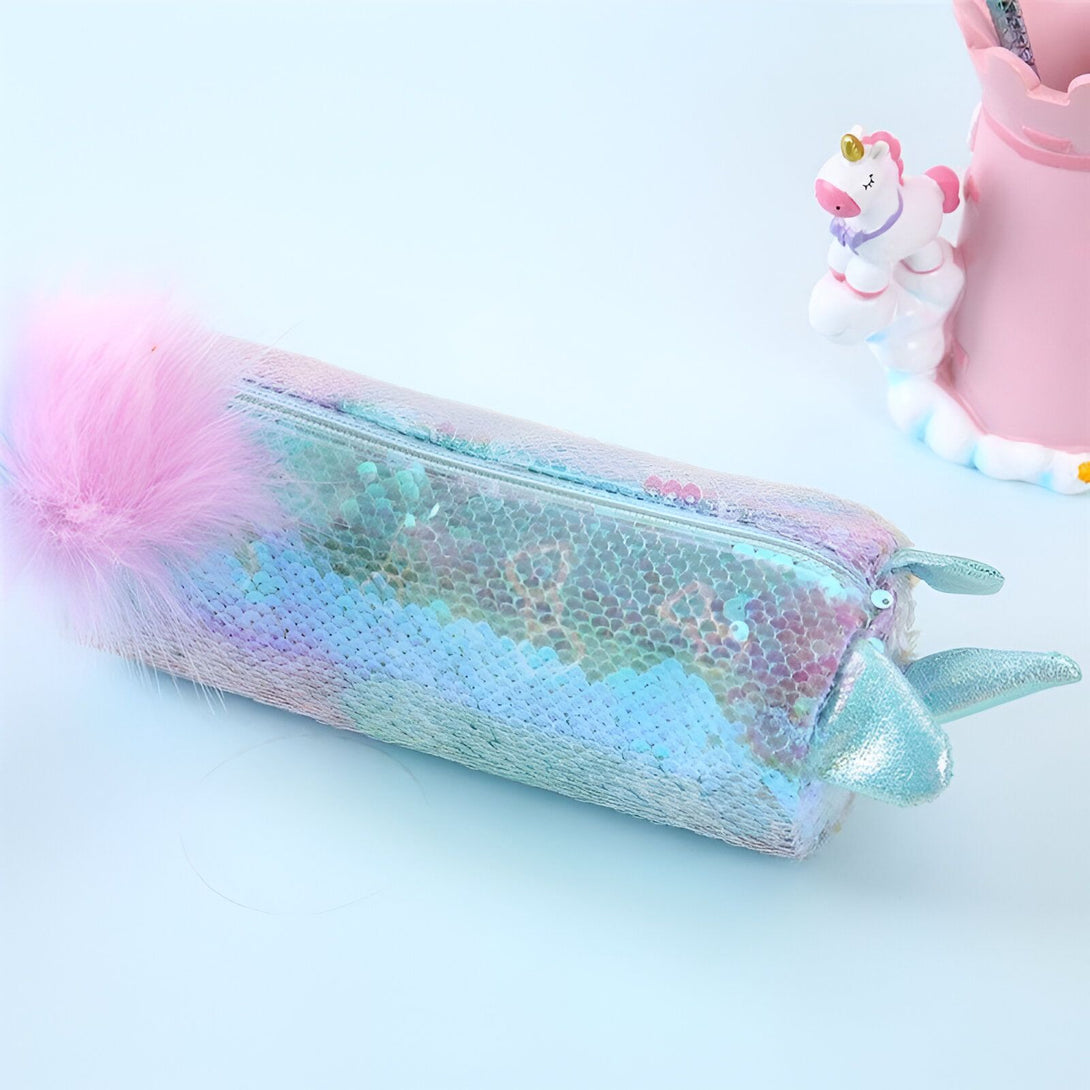 Une trousse à crayons en forme de queue de sirène avec des paillettes réversibles et une fermeture éclair. La trousse est rose et bleue avec une queue de sirène en peluche rose à une extrémité et une corne de licorne en peluche bleue à l'autre.