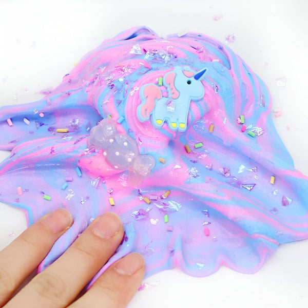 Gros plan d'une main manipulant une pâte à modeler (slime) aux couleurs pastel bleu, rose et violet. Décorations : licorne, bonbon transparent et paillettes multicolores., 45501394845951 | Licorne Shop