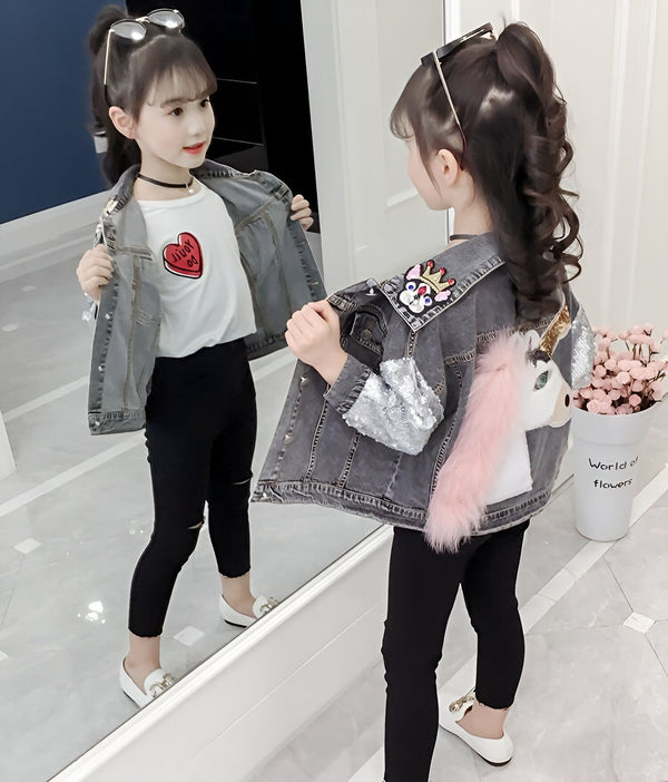 Fille avec une veste en jean décorée, se regardant dans un miroir. Elle porte un t-shirt blanc avec un cœur rouge, un pantalon noir et des chaussures blanches. Sa veste a un motif de chien couronné et une licorne avec une queue rose., 45501803921663,45501803954431,45501803987199,45501804019967,45501804052735,45501804085503,45501804118271,45501804151039 | Licorne Shop