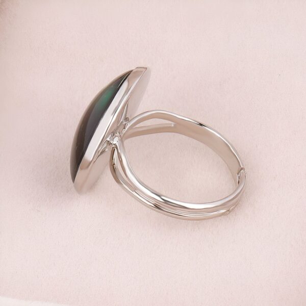 Une bague en argent avec une pierre ovale verte sertie sur le dessus. La bague est ouverte et réglable.