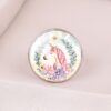 L'image représente un bouton de meuble rond en verre avec un motif de licorne. La licorne est blanche avec une crinière et une queue roses. Elle est entourée de fleurs et de feuilles.