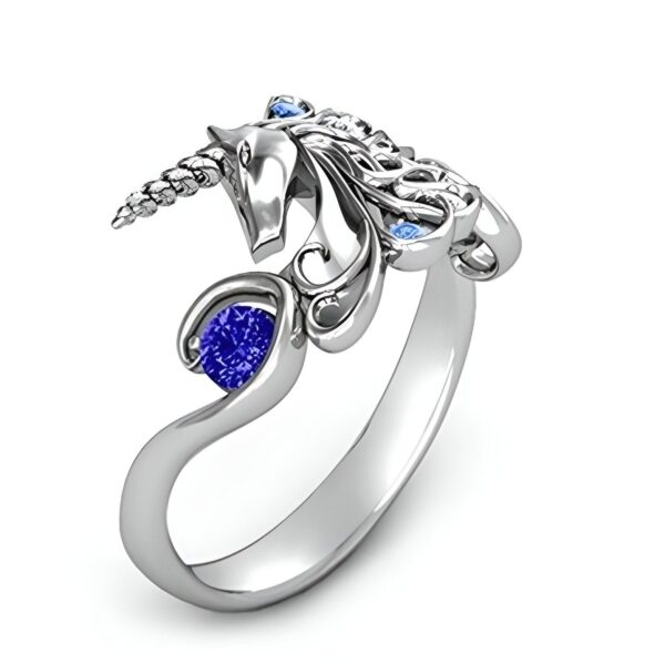 bague-licorne-zirconium-bleu-2a.jpg Une bague en argent avec une pierre précieuse bleue et des accents de pierres précieuses bleues plus petites. La bague est en forme de licorne avec la tête de la licorne tournée vers le haut et la queue enroulée autour de son corps.