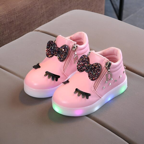 Une paire de chaussures roses pour enfant avec des nœuds pailletés et des lumières LED dans les semelles.