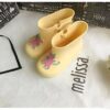 Paire de bottes de pluie jaunes Mini Melissa pour enfants, avec un motif de cheval rose et bleu. Elles sont sur un tissu blanc à côté de leur boîte., 45501099376895,45501099409663,45501099442431,45501099475199,45501099507967,45501099540735,45501099573503,45501099606271,45501099639039 | Licorne Shop