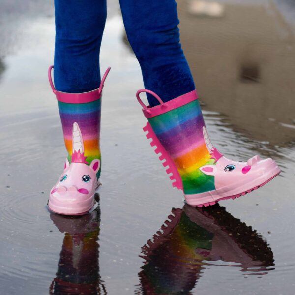 bottes-impermeables-licorne-pour-enfant-taille-12-1a.jpg Enfant portant des bottes de pluie arc-en-ciel à motif de licorne dans une flaque d'eau. Bottes roses avec des détails de licorne et des poignées roses. Pantalon bleu. Reflet dans l'eau., 45501218652415,45501218685183,45501218717951,45501218750719,45501218783487,45501218816255,45501218849023,45501218881791,45501218914559 | Licorne Shop