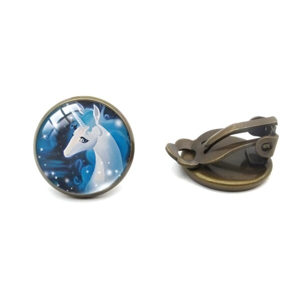 boucles-d-oreilles-licorne-femme-elegante-clip-2a.jpg Une paire de boucles d'oreilles en bronze avec un cabochon en verre rond représentant une licorne blanche et ailée sur un fond bleu nuit étoilée.