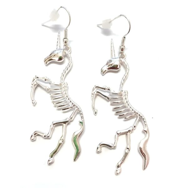 boucles-d-oreilles-pendantes-licorne-squelette-fantaisie-1a.jpg Paire de boucles d'oreilles pendantes en forme de squelette de licorne argenté, présentées sur un fond blanc uni. Bijoux originaux pour les passionnés de créatures fantastiques et d'accessoires insolites., 45502397710591 | Licorne Shop