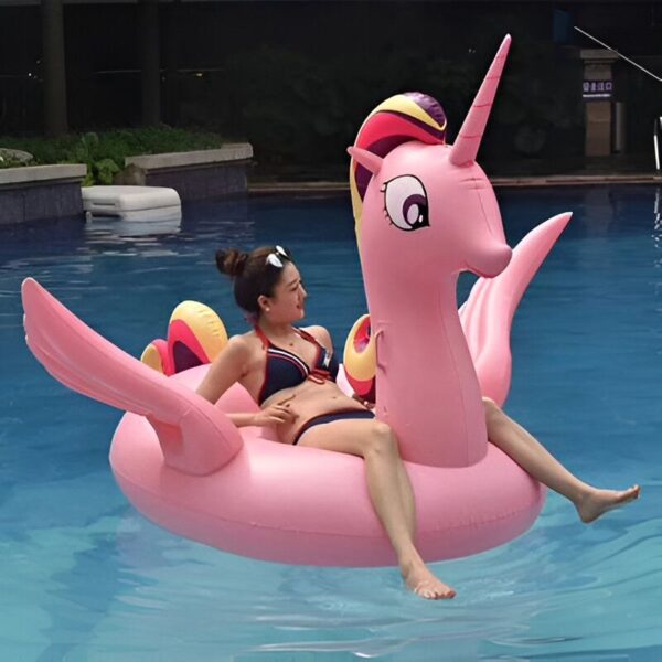 bouee-geante-licorne-2-places-1a.jpg Une femme en bikini se détend sur une bouée gonflable rose en forme de licorne dans une piscine. Le ciel est dégagé et l'eau est bleue., 45501251682559 | Licorne Shop