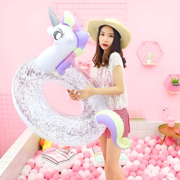 bouee-gonflable-licorne-geante-1a.jpg Une jeune femme en chapeau de paille tient une bouée gonflable licorne scintillante dans un décor rose pastel avec des balles roses et blanches., 45501244244223 | Licorne Shop
