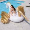 Une femme en maillot de bain blanc assise sur une bouée licorne ailée dorée au bord d'une piscine bleue. Elle porte des lunettes roses et regarde la caméra. Ambiance estivale et joyeuse., 45501245686015 | Licorne Shop