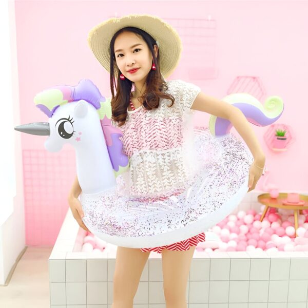 bouee-gonflable-licorne-sun-squad-pour-piscine-1a.jpg Jeune femme souriante avec un chapeau de paille, portant un flotteur licorne pailleté, sur fond rose., 45501250044159 | Licorne Shop