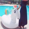 bouee-licorne-geante-pour-piscine-1a_e4b4bdda-a4f7-4d9c-a27b-88fee44b1ead.jpg Femme près d'une piscine avec une bouée gonflable licorne blanche à crinière arc-en-ciel. Elle porte une robe bleue foncée et un chapeau rayé., 45501250732287 | Licorne Shop