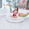 Jeune femme en maillot de bain rouge assise sur une bouée licorne gonflable dans une piscine à balles blanches. Décoration tropicale en arrière-plan., 45501227892991 | Licorne Shop