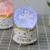 Boule à neige musicale licorne scintillante. Objet de décoration avec une licorne blanche à l'intérieur d'une boule transparente remplie de paillettes, posée sur un socle blanc décoré d'étoiles et de l'inscription "Twinkle twinkle little star"., 45501133816063 | Licorne Shop