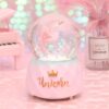 Boule à neige rose avec licorne à l'intérieur. Décoration avec un mini piano, un vase rose et une inscription "Unicorn" avec une couronne. Idéal pour chambre d'enfant ou cadeau fantaisie., 45501133881599 | Licorne Shop