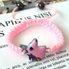 Un bracelet rose avec un pendentif licorne en émail. La licorne est rose avec une crinière et une queue arc-en-ciel. Le bracelet est fait de corde tressée rose.