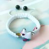 Un bracelet en corde blanche avec un pendentif licorne en métal émaillé. La licorne est blanche avec une crinière et une queue arc-en-ciel.