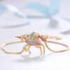 bracelet-licorne-en-zircone-cubique-9a.jpg L'image montre un bracelet en or avec un pendentif licorne. La licorne est sertie de pierres précieuses roses, bleues et vertes. Le bracelet est porté sur un poignet de femme.