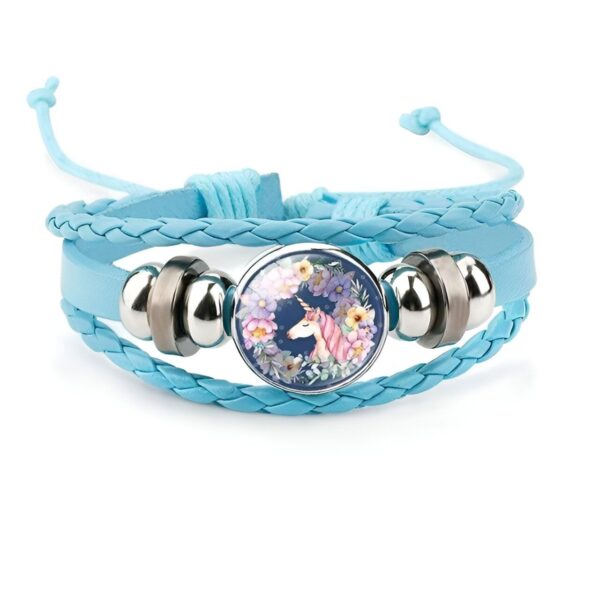 bracelet-licorne-enfant-tresse-2a.jpg Le bracelet est en cuir tressé bleu avec un fermoir en acier inoxydable. Il est décoré d'une perle en verre avec une image d'une licorne blanche avec des fleurs roses et bleues.