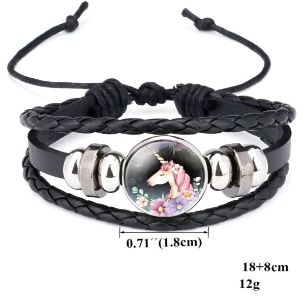 bracelet-licorne-enfant-tresse-6a.jpg Le bracelet est en cuir tressé noir avec un fermoir en acier inoxydable. Il est orné d'une perle en verre avec une image d'une licorne blanche avec une crinière et une queue roses. La licorne est entourée de fleurs roses, violettes et bleues. Le bracelet mesure 18 cm de long et 8 cm de large. Il pèse 12 grammes.