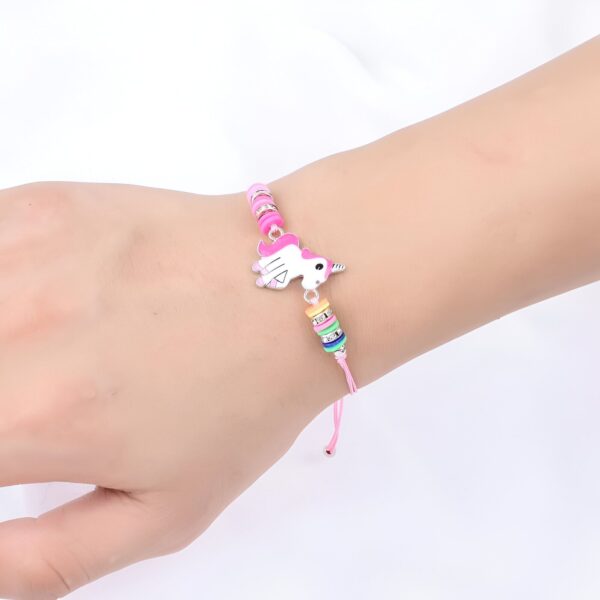 bracelet-licorne-rose-femme-1a Un bracelet rose avec une breloque licorne blanche et rose. La licorne a une crinière et une queue arc-en-ciel. Le bracelet est porté par une main d'enfant.