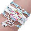 bracelet-licorne-tresse-fille-3a.jpg L'image montre un bracelet avec un pendentif en forme de licorne. La licorne est blanche avec une crinière et une queue arc-en-ciel. Le bracelet est en cuir tressé de couleur bleue et blanche. Il est agrémenté de perles en argent et d'un fermoir en forme de nœud.