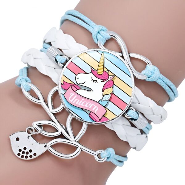 bracelet-licorne-tresse-fille-3a.jpg L'image montre un bracelet avec un pendentif en forme de licorne. La licorne est blanche avec une crinière et une queue arc-en-ciel. Le bracelet est en cuir tressé de couleur bleue et blanche. Il est agrémenté de perles en argent et d'un fermoir en forme de nœud.