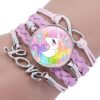 bracelet-licorne-tresse-fille-6a.jpg L'image montre un bracelet en cuir tressé rose avec un pendentif en forme de licorne. La licorne est blanche avec une crinière et une queue arc-en-ciel. Elle porte un collier avec un pendentif en forme de cœur. Le bracelet est également décoré de perles en forme d'étoile et de lune.