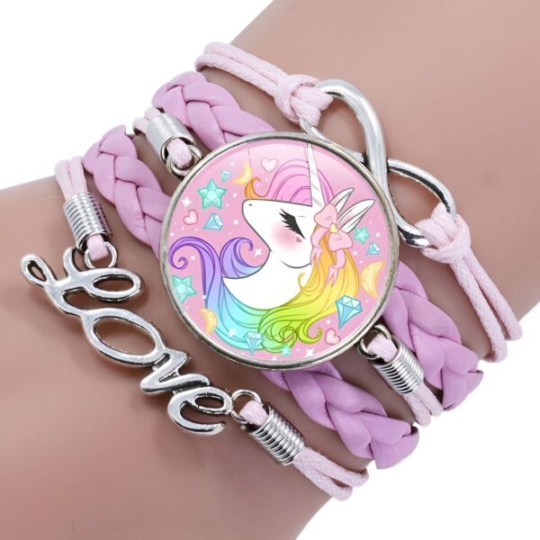 bracelet-licorne-tresse-fille-6a.jpg L'image montre un bracelet en cuir tressé rose avec un pendentif en forme de licorne. La licorne est blanche avec une crinière et une queue arc-en-ciel. Elle porte un collier avec un pendentif en forme de cœur. Le bracelet est également décoré de perles en forme d'étoile et de lune.