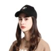 casquette-licorne-adulte-noir-1a.jpg Une jeune femme porte une casquette noire avec une licorne brodée sur le devant. La licorne a une crinière et une queue arc-en-ciel. La femme a les cheveux longs et bruns et un maquillage léger. Elle porte un sweat-shirt beige.