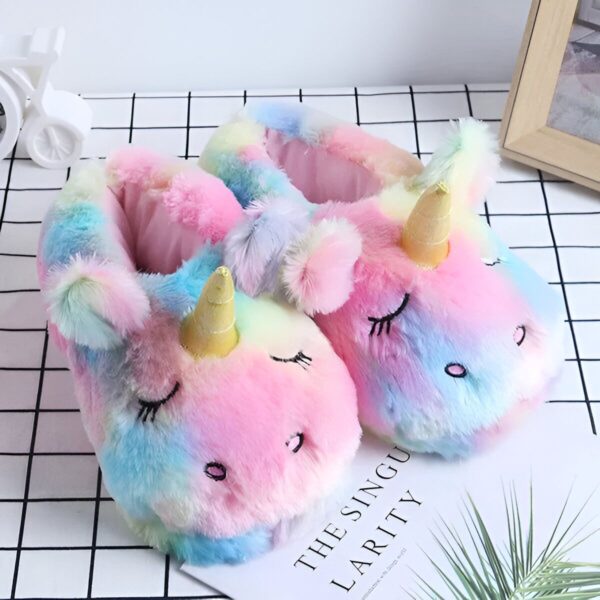Une paire de pantoufles licorne en peluche arc-en-ciel avec une corne dorée et des yeux fermés.