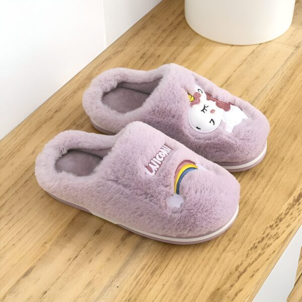 chausson-licorne-petite-fille-violet-1a.jpg Une paire de pantoufles licorne en peluche violette avec un arc-en-ciel et le mot "licorne" brodés dessus.