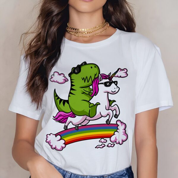 chemise-originale-a-motifs-licorne-et-dinosaure-1a.jpg Femme portant un T-shirt blanc avec un dinosaure vert et une licorne blanche, tous deux portant des lunettes de soleil, chevauchant un arc-en-ciel avec des nuages. Colliers dorés à son cou., 45502330274047,45502330306815,45502330339583,45502330372351,45502330405119,45502330437887,45502330470655,45502330503423 | Licorne Shop