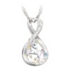 L'image représente un pendentif en forme de cœur avec une licorne blanche incrustée de cristaux multicolores. La licorne a une crinière et une queue roses et violettes. Le pendentif est en métal argenté et est suspendu à une chaîne en argent.