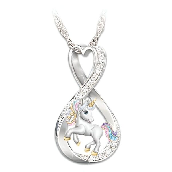 L'image représente un pendentif en forme de cœur avec une licorne blanche incrustée de cristaux multicolores. La licorne a une crinière et une queue roses et violettes. Le pendentif est en métal argenté et est suspendu à une chaîne en argent.