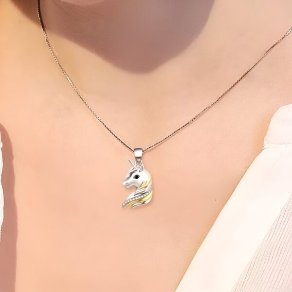 collier-licorne-anniversaire-2a.jpg L'image montre un pendentif en forme de tête de licorne en argent et or avec une chaîne en argent. La licorne a une crinière et une queue en or et des yeux noirs. Le pendentif est porté par une femme avec un haut blanc.