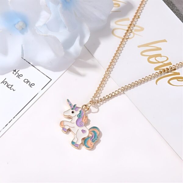L'image représente un collier avec un pendentif en forme de licorne. La licorne est blanche avec une crinière et une queue arc-en-ciel. Le collier est en métal doré.