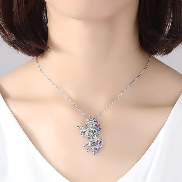 collier-licorne-fantaisie-1a.jpg L'image montre un collier avec un pendentif licorne. La licorne est sertie de cristaux multicolores et a une crinière et une queue arc-en-ciel. Le collier est en argent sterling.