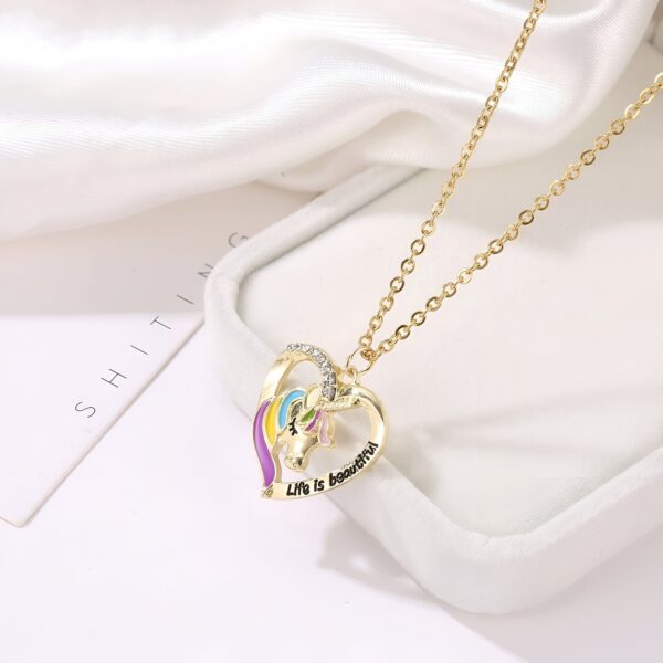 Un collier avec un pendentif en forme de cœur. Le pendentif est doré et contient une licorne colorée. Il est écrit "life is beautiful" en anglais sur le pendentif.