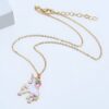 collier-licorne-fille-2a.jpg Un collier avec un pendentif licorne en émail coloré. La licorne est blanche avec une crinière et une queue arc-en-ciel. Elle est debout sur ses pattes arrière et a une expression joyeuse sur son visage. Le collier est en métal doré et la chaîne est réglable.