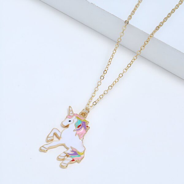 collier-licorne-fille-3a.jpg L'image représente un collier avec un pendentif en forme de licorne. La licorne est blanche avec une crinière et une queue arc-en-ciel. Le collier est en métal doré.