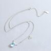 collier-licorne-fille-elegance-3a.jpg L'image représente un collier avec deux pendentifs. Le pendentif du haut est une pierre précieuse ovale de couleur claire et le pendentif du bas est un arc-en-ciel coloré. La chaîne est en argent.