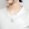 collier-licorne-geometrique-1a.jpg Une image d'une femme portant un collier avec un pendentif en forme de tête de licorne. La licorne est représentée de profil et est faite de métal argenté. La femme a les cheveux noirs et porte un t-shirt blanc.
