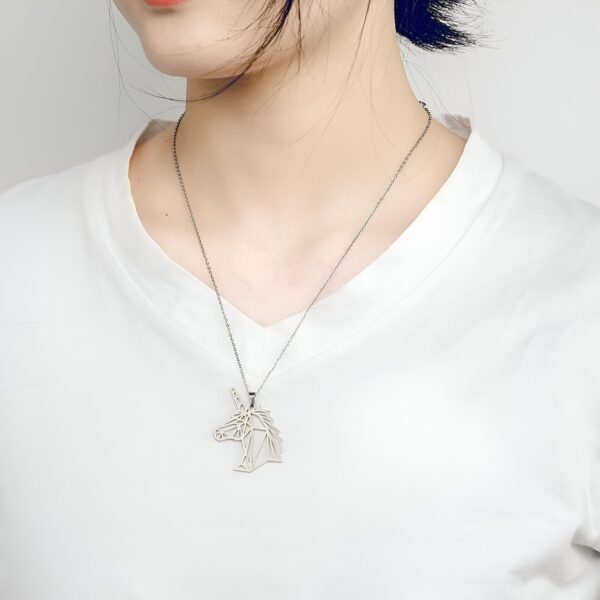 Une image d'une femme portant un collier avec un pendentif en forme de tête de licorne. La licorne est représentée de profil et est faite de métal argenté. La femme a les cheveux noirs et porte un t-shirt blanc.
