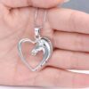 Un pendentif en forme de cœur avec un cheval à l'intérieur. Le cheval est représenté de profil et est en argent. Le pendentif est porté par une main.