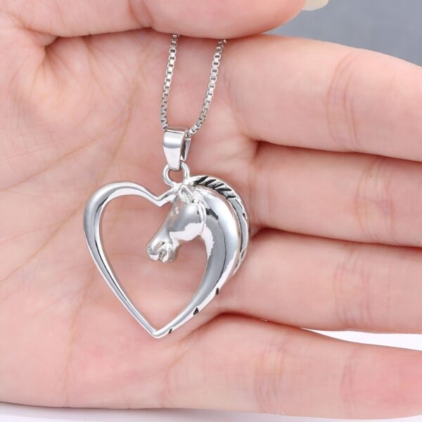 Un pendentif en forme de cœur avec un cheval à l'intérieur. Le cheval est représenté de profil et est en argent. Le pendentif est porté par une main.