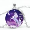 collier-licorne-lune-1a.jpg Un pendentif en forme de cercle avec une image d'une licorne blanche cabrée sur un fond violet avec une lune et des sapins enneigés.